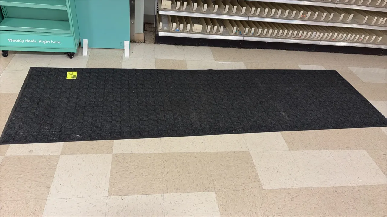 Commercial floor runner rug. Features a dark charcoal gray textured waffle-pattern surface with rubber backing and beveled border. 10'L.