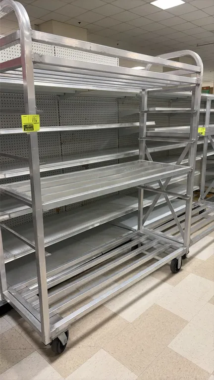 Aluminum 3-tier portable rack. Features slatted aluminum construction and 3 storage levels. 60" x 24" x 78". Mounted on casters. Shelving in backgroun
