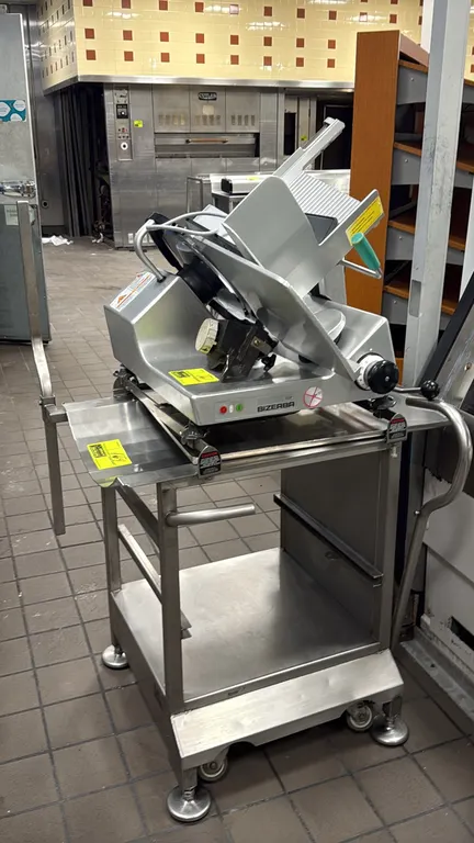 Face to Face stainless steel portable slicer stand. Features lower undershelf, side handles, and retractable caster lift mechanism. Mounted on casters
