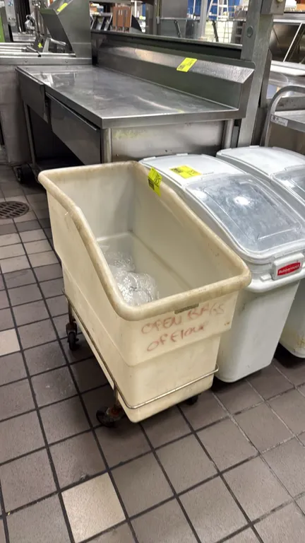 Remcon mobile poly ingredient bin. Features molded white polyethylene construction and a slanted opening. Mounted on a metal dolly base with casters.