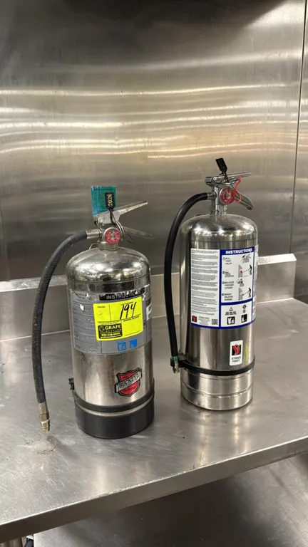 Buckeye and Strike First wet chemical fire extinguishers. Features stainless steel cylinders, discharge hoses, operating levers with pull pins, and pr