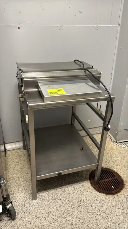 Stainless steel 3-roll film wrapper station. Features an integrated heated seal plate, film cut-off bar, multiple film roll support brackets, and a st