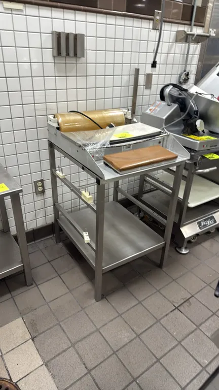 Heat Seal 3-roll film wrapper. Features a heated sealing plate, film cut-off bar, and stainless steel construction. Mounted on a stainless steel stand