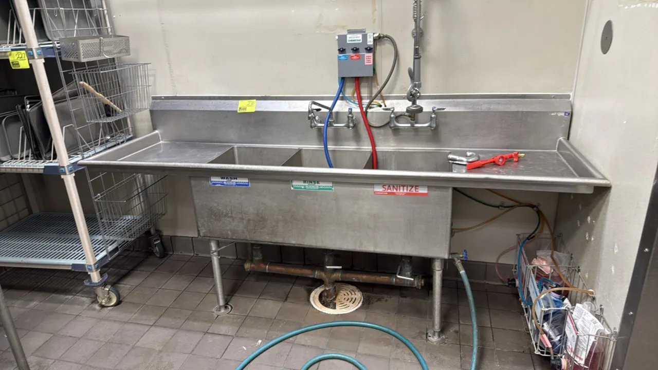 Stainless steel 3-compartment sink. Features left and right drainboards, integrated backsplash, splash-mount faucet with swing spout, pre-rinse spray