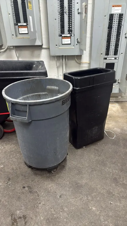 Rubbermaid poly trash cans. Includes a gray BRUTE round trash container mounted on a rolling dolly base with swivel casters, and a black slim rectangu