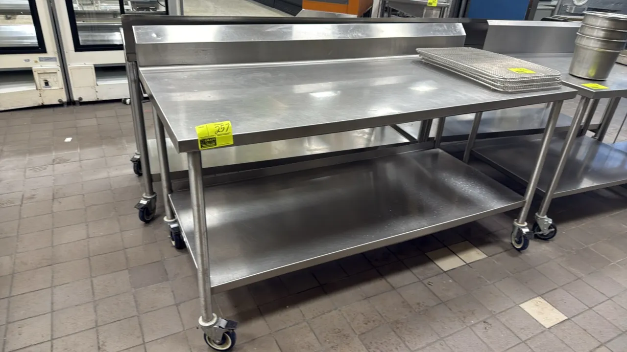 Stainless steel work table. Features a rear backsplash and lower undershelf. 72"L x 30"W. Mounted on swivel casters. Contents not included.