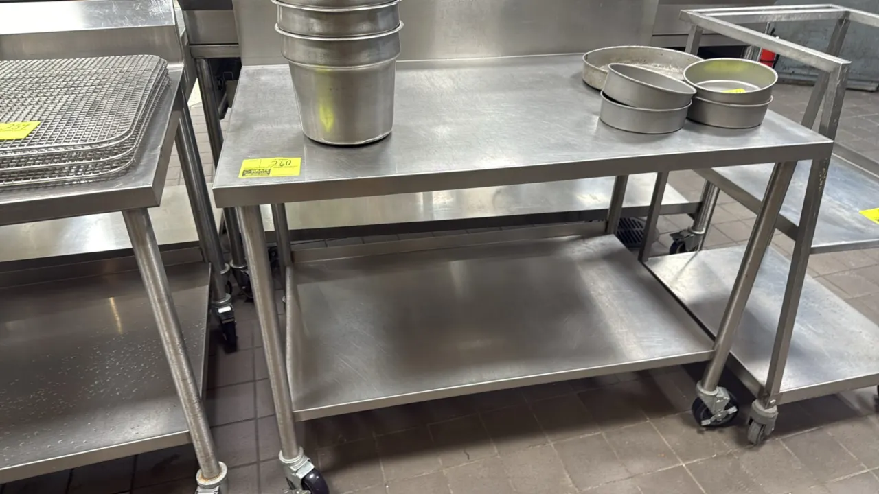 Stainless steel work table. Features an integrated backsplash and lower undershelf. 48"L x 30"W. Mounted on swivel casters. Contents not included.