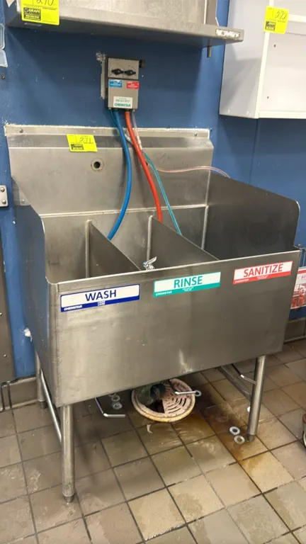 Stainless steel 3-compartment sink. Features integrated backsplash, side splashes, and lever waste drains. Includes detached faucet assembly and plumb