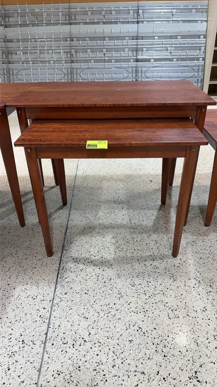 Set of (2) wood nesting display tables. Features tapered legs and a warm wood finish. Dimensions: 48"L and 36"L.