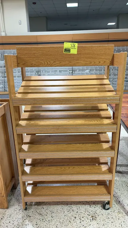 Portable bakery display rack. Features woodgrain laminate construction with 5 tiered slatted shelves and front shelf lips. Mounted on casters.