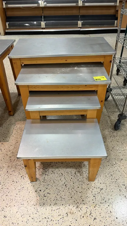 Set of (4) assorted nesting display tables. Features metal top surfaces and solid wood frames with tapered legs. Designed to nest or display in tiered