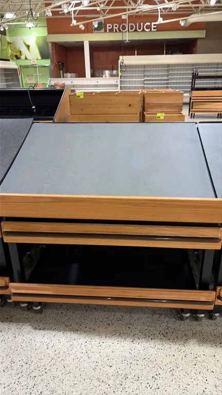Produce tilt tables. Features slanted display deck, wood-look trim with protective bumper rails, and black metal frame. 4'L. Mounted on casters.