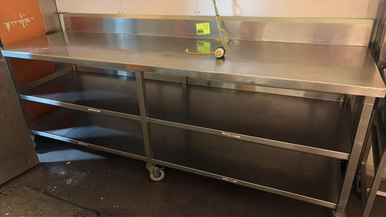 Stainless steel work table. Features an integrated backsplash and double undershelves. Dimensions: 96" x 29". Mounted on square tubular legs. Hanging