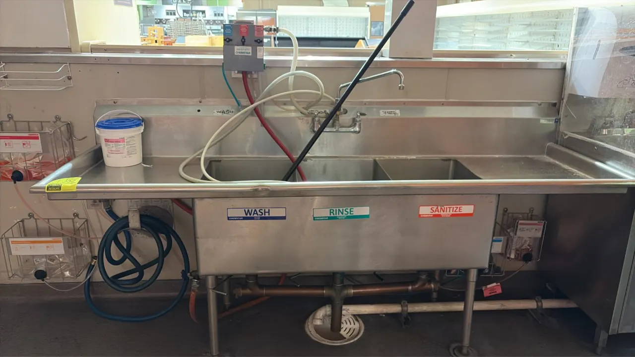 Stainless steel 3-compartment sink. Features left and right drainboards, splash-mount faucet with swing spout, and Chemstar chemical dispensing system