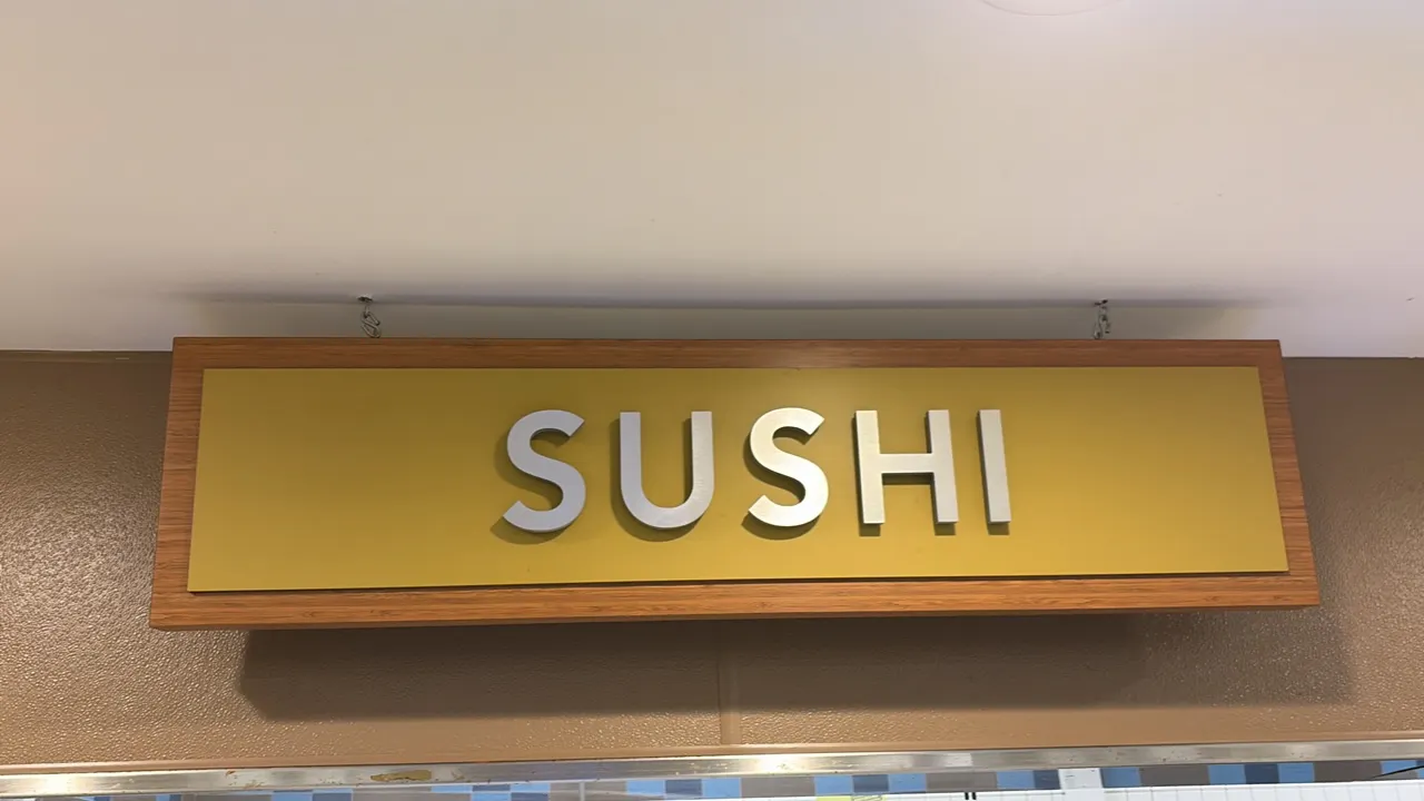 Hanging retail "SUSHI" department sign. Features dimensional raised lettering on a yellow background panel with a woodgrain-style border frame. Ceilin