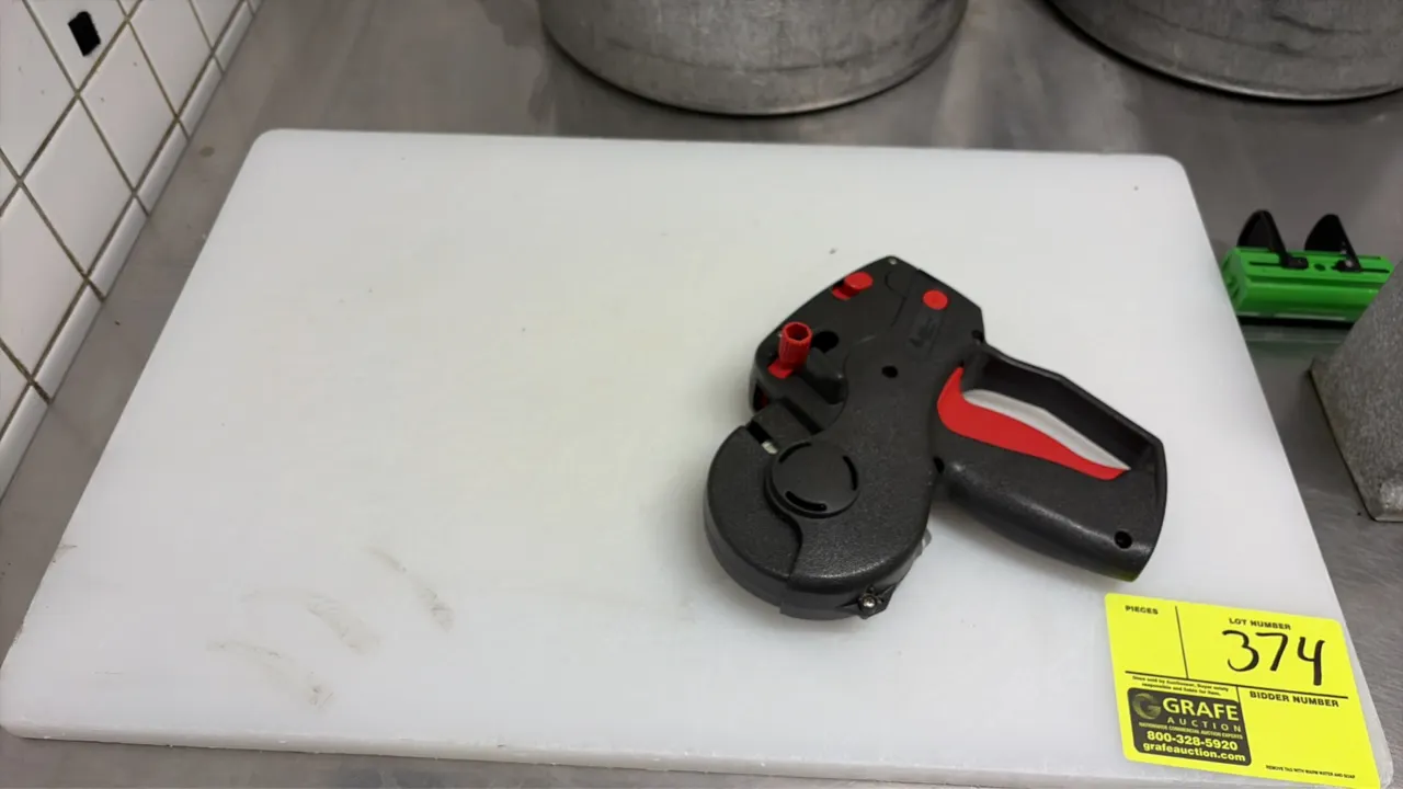 White poly cutting board with handheld label gun. Features a white polyethylene cutting surface and a manual handheld price and date labeling gun.