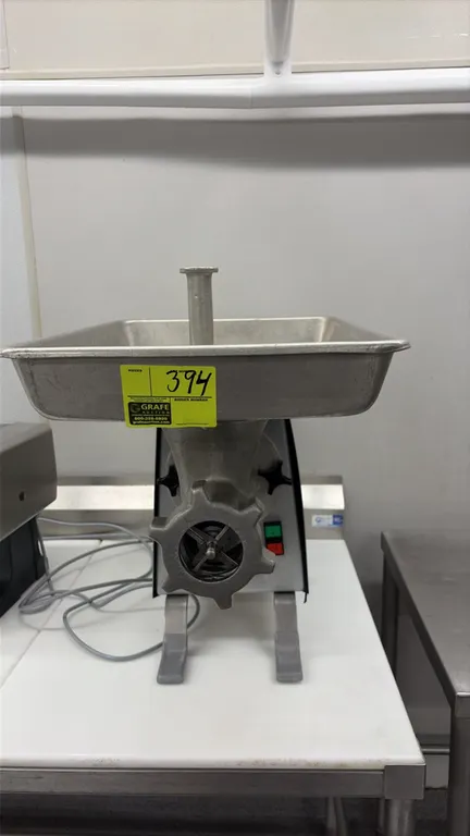 2013 Univex MG 22 tabletop meat grinder. Features stainless steel housing, feed tray with safety guard, feed stomper, and push-button controls. Table