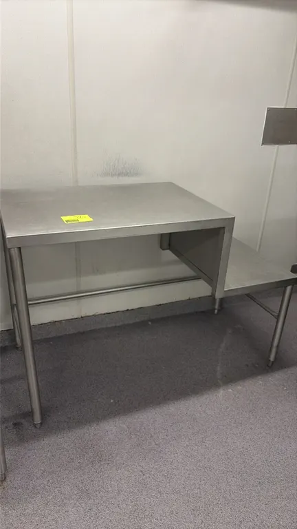 Stainless steel grinding table. Features an elevated main work surface with an integrated step-down lower platform for lugs or containers, tubular cro
