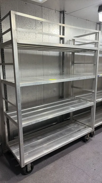 Aluminum 4-tier mobile shelving cart. Features slatted shelves and top tier retaining rails. 5'L. Mounted on casters.