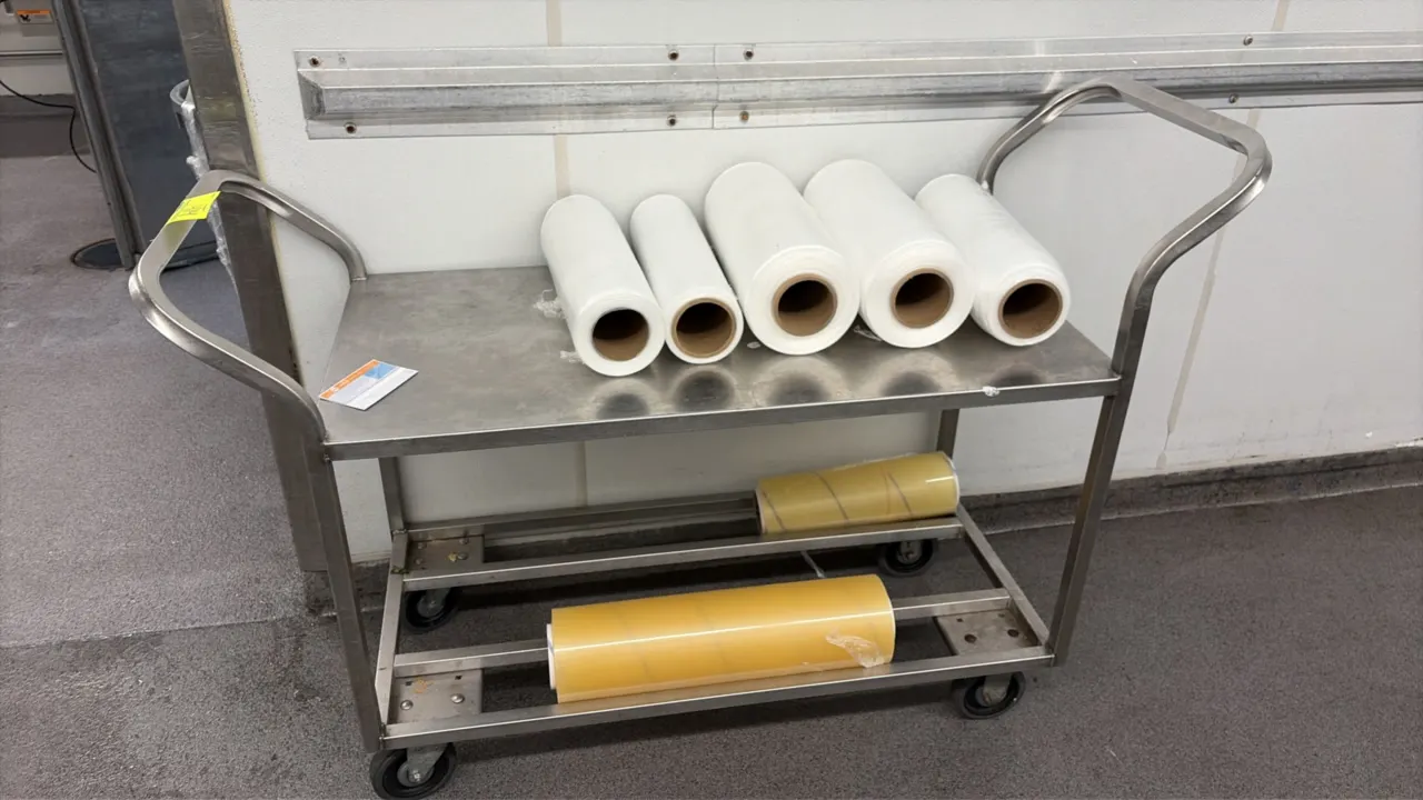Stainless steel utility cart. Features dual tubular push handles, a solid top shelf, and an open lower shelf. Includes assorted rolls of plastic packa