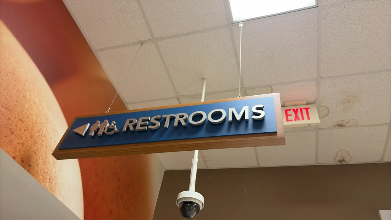 Hanging restroom directional sign. Features wood-look frame backer with blue face panel, dimensional 'RESTROOMS' lettering, directional arrow, and pic