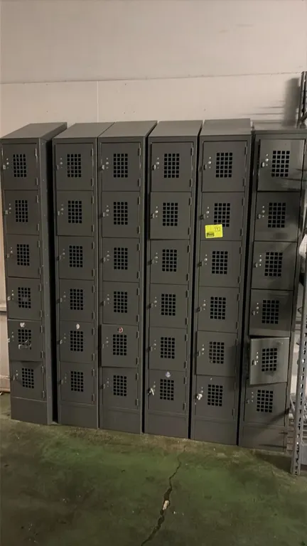 Metal employee lockers. Features 6-tier compartment configuration, square-perforated ventilated doors, padlock hasps, and a gray finish. Sloped top ho