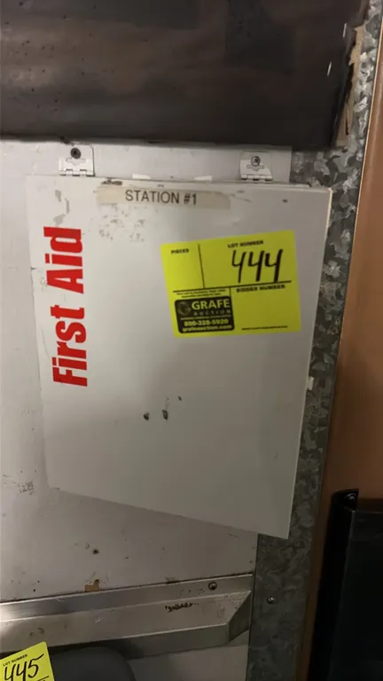 Wall-mount first aid cabinet. Features white metal casing with hinged door, internal divided plastic organizer compartments, and wall mounting bracket