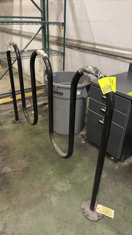 Metal wave bike rack. Features tubular metal construction with a black finish and a 3-loop wave design. Equipped with round surface-mount base plates