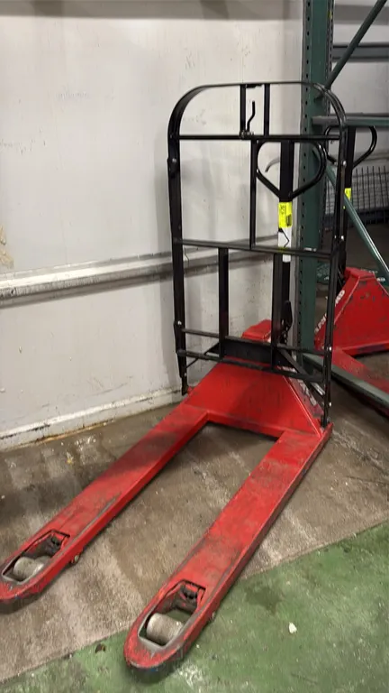 Raymond manual pallet jack. Features red steel frame construction, attached tall load backrest extension, loop steering and pump handle, and polyureth