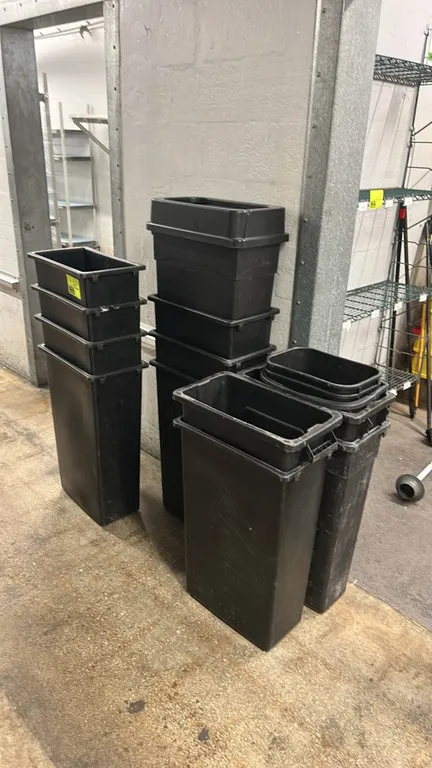 Assorted poly slim trash bins. Features durable black plastic construction, slim space-saving design, and integrated rim handles. Includes multiple st
