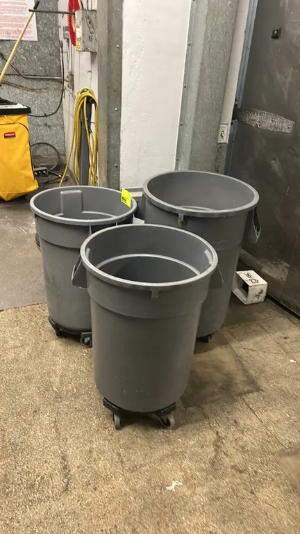 Poly bulk trash bins with transport dollies. Features gray molded polyethylene construction with integrated side handles. Each bin is mounted on a mob