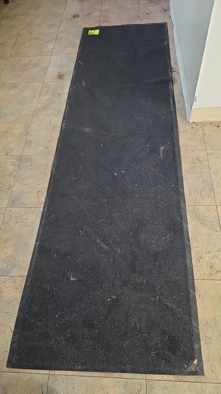 Rubber-backed floor runner mat. Features a dark charcoal carpet surface with beveled rubber edging. Approx. 33"W x 113"L.