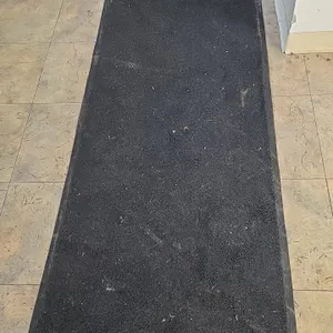 Rubber-backed floor runner mat. Features a dark charcoal carpet surface with beveled rubber edging. Approx. 33"W x 113"L.
