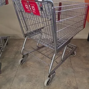 Conventional wire shopping cart. Features a folding child seat with safety strap, red plastic handle cover, red corner bumpers, and a lower storage tr