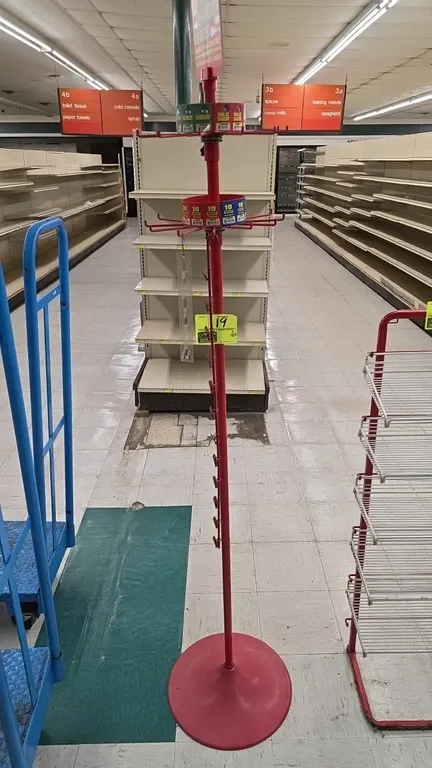 Metal rotating merchandiser display rack. Features red painted finish, 2 spinning wire hook tiers, center pole clip strip hangers, round base, and top