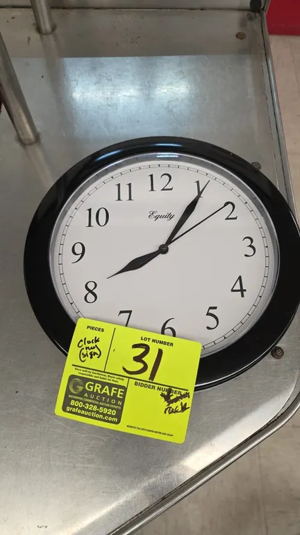 Equity 25203 battery-operated wall clock. Features a black plastic frame and white dial with Arabic numerals. 9.75" Dia. Battery operated. Rear keyhol