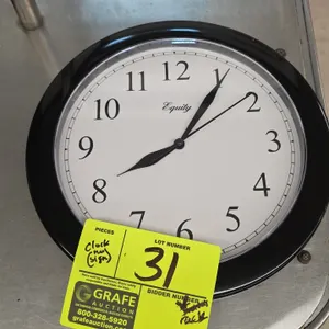 Equity 25203 battery-operated wall clock. Features a black plastic frame and white dial with Arabic numerals. 9.75" Dia. Battery operated. Rear keyhol