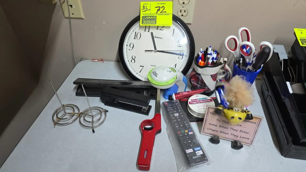 Assorted office supplies. Includes Advance quartz wall clock, Dymo embossing label maker, desktop 3-hole punch, stapler, receipt spindles, Sanyo TV re