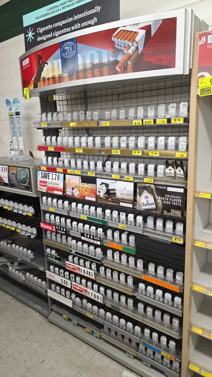 Metal frame tobacco display merchandiser. Features overhead graphic display header canopy, wire grid backing, adjustable shelving equipped with spring