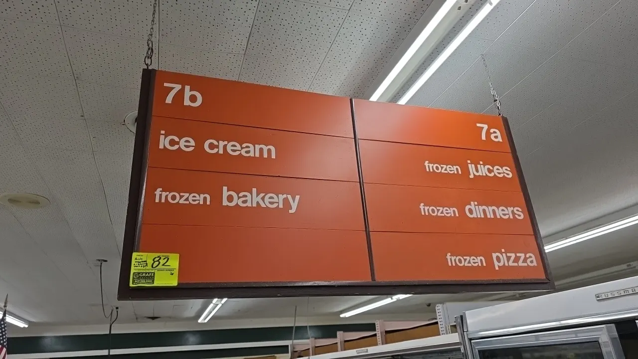Wood frame double-sided hanging aisle markers. Features orange directional panels with white lettering and aisle numbering, dark wood frames, and top