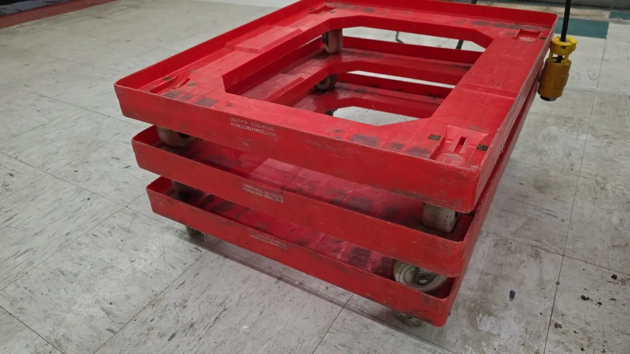 Poly bread tray dollies. Features molded red plastic construction with an open-center frame and perimeter lip. 22.5" x 27.5". Mounted on 4 swivel cast
