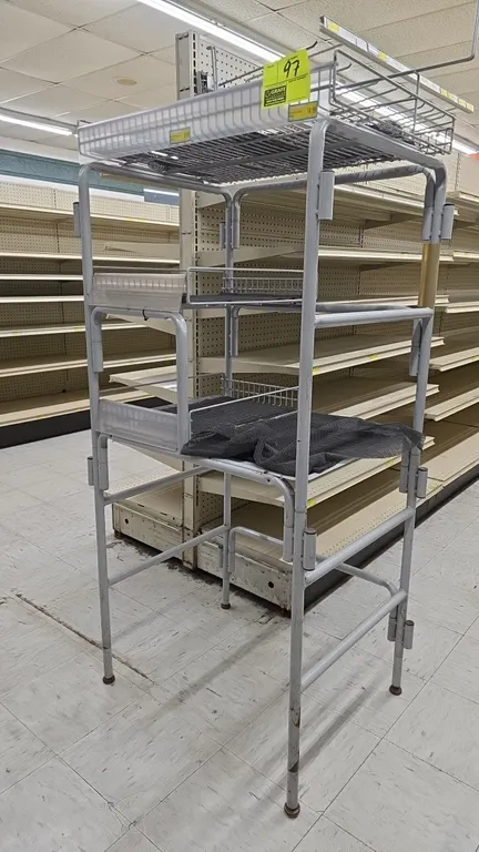 Gray metal merchandiser display rack. Features tubular metal construction, tiered wire basket shelves, clear front product retainers with label channe