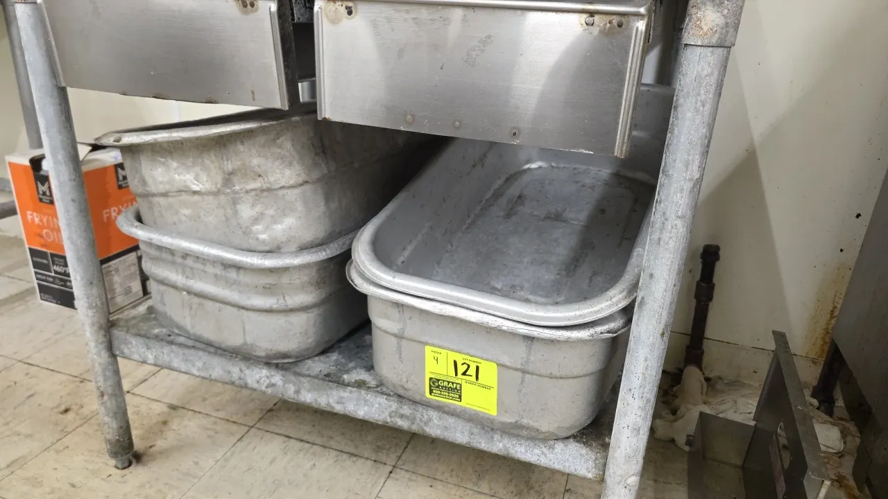 Aluminum meat lugs. Features seamless aluminum construction with rolled rims and a nesting design. Note: Units exhibit dents. Table and surrounding it