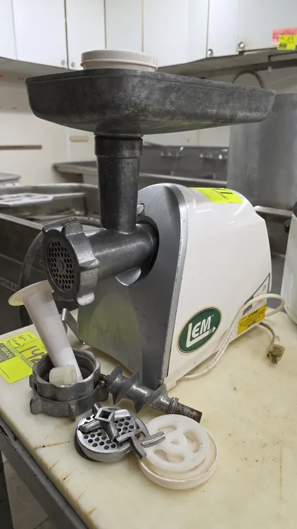 LEM 822 #8 electric meat grinder. Features top feed tray, plastic stomper, auger, grinding plates, cutting blades, sausage stuffing tube, and black po