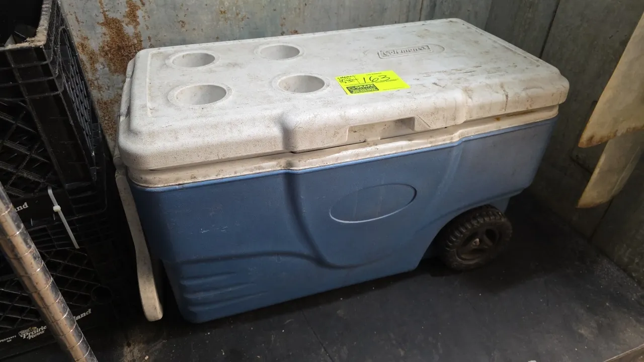 Coleman wheeled cooler. Features hinged lid with four molded cup holders, integrated lid ruler, tow handle, and two rear wheels.