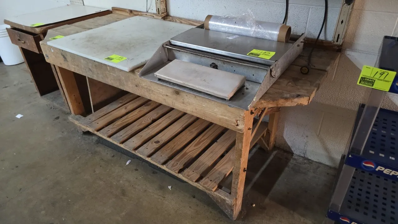 Wood work table. Features a wood top with rear backsplash and a slatted lower shelf. 6' x 2'6". Tabletop items and contents not included.