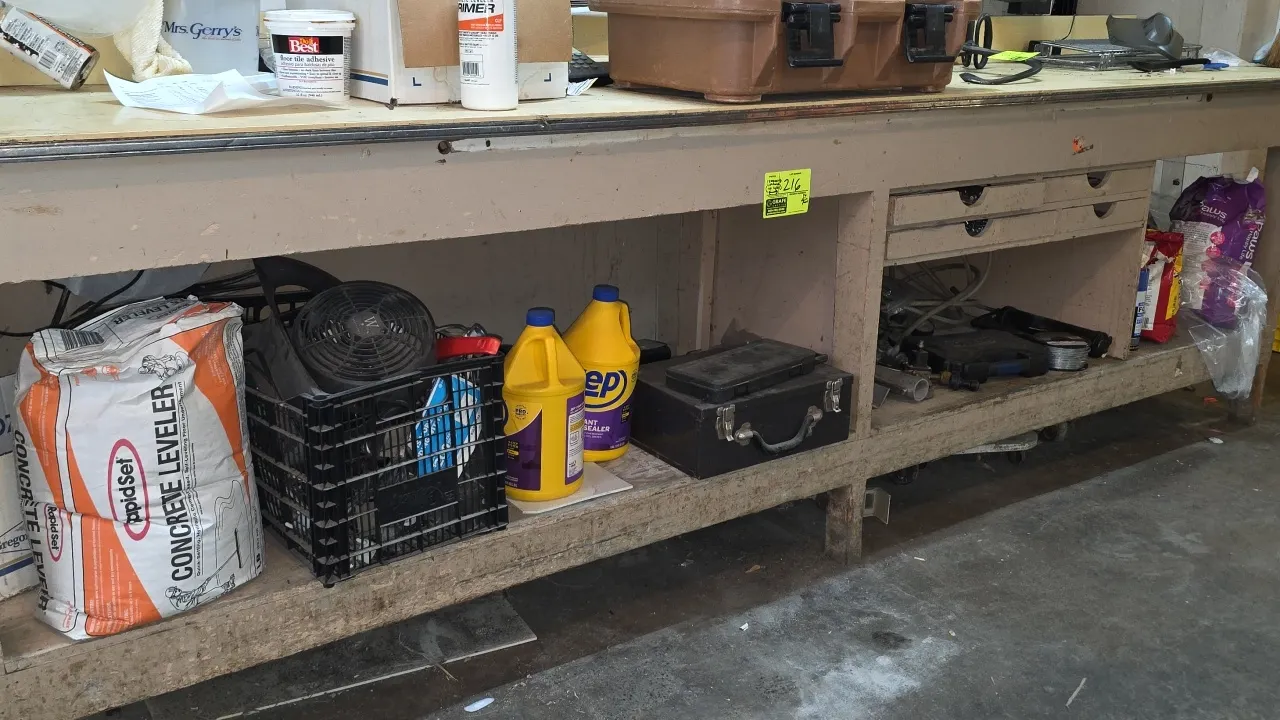 Assorted workbench lower shelf contents. Includes socket set, DeWalt cordless drill, drill bit set, metal toolbox, fasteners, grease gun, wire spool,