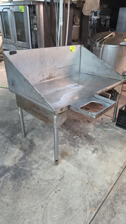 Stainless steel soiled dish table. Features a three-sided splash guard and extended front scrap cutout. 48" x 30" x 25". Mounted on tubular legs. Note