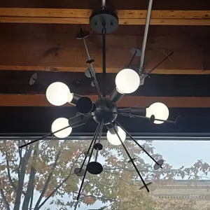 Metal sputnik-style chandelier. Features a matte black finish, multi-directional radiating arms with decorative disc accents, (6) light sockets, and c