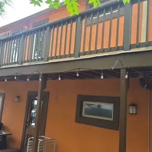 Outdoor LED string lights. Features black cord with suspended drop sockets and clear Edison-style LED filament bulbs. Railing, patio structure, umbrel